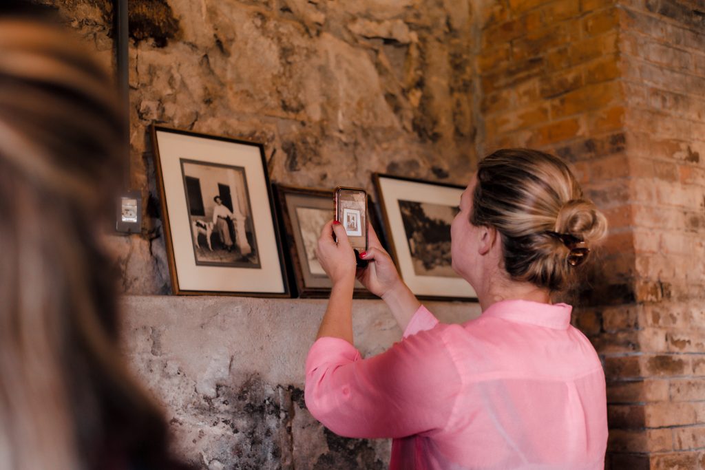 Moça tira foto de retratos antigos em visita de enoturismo na vinícola